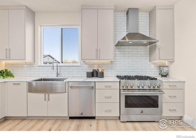 kitchen with tasteful backsplash, light stone countertops, wall chimney range hood, and appliances with stainless steel finishes