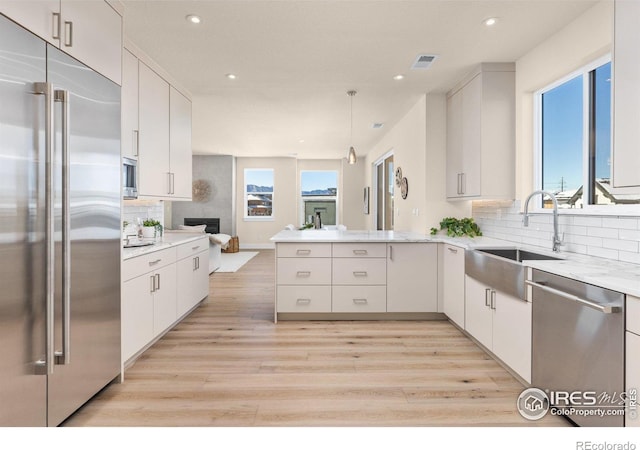 kitchen featuring white cabinets, built in appliances, kitchen peninsula, and hanging light fixtures