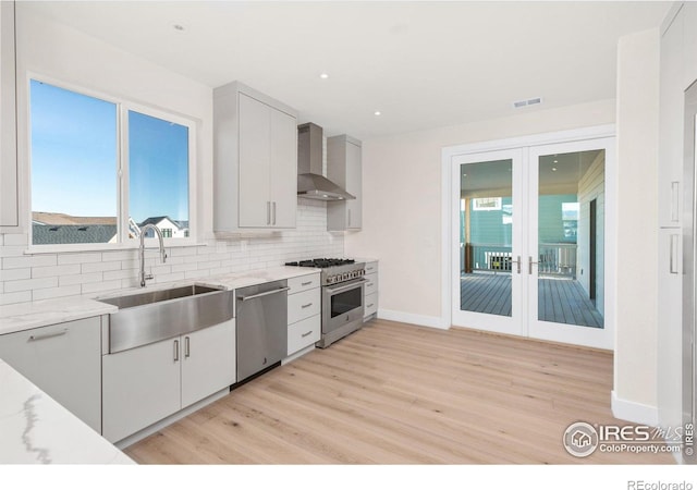 kitchen featuring backsplash, sink, wall chimney exhaust hood, light stone countertops, and stainless steel appliances