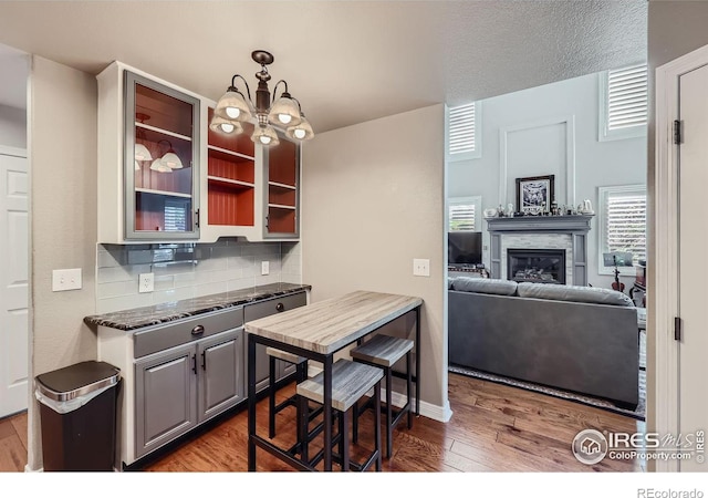 kitchen with hanging light fixtures, tasteful backsplash, dark hardwood / wood-style flooring, dark stone counters, and gray cabinets