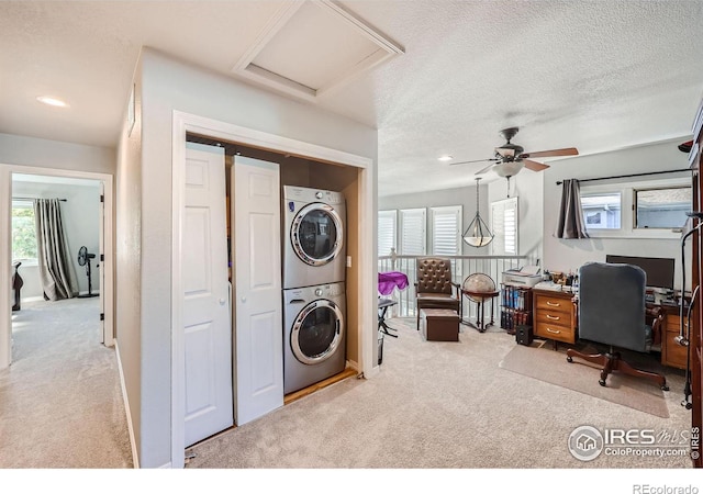 laundry room with stacked washer / drying machine, ceiling fan, light colored carpet, and a textured ceiling