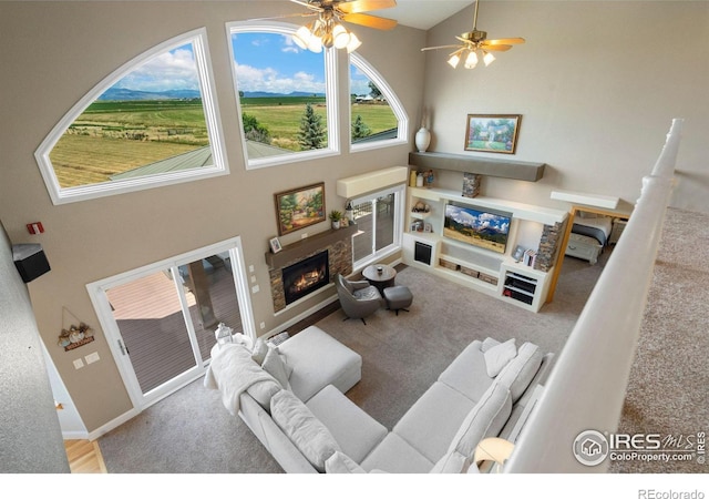 carpeted living room featuring a stone fireplace, ceiling fan, and a towering ceiling