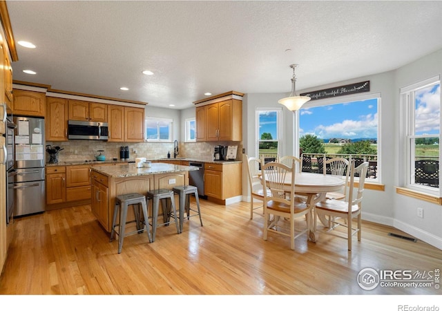 kitchen with hanging light fixtures, light stone counters, appliances with stainless steel finishes, a kitchen island, and light wood-type flooring