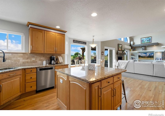 kitchen featuring light wood-type flooring, sink, dishwasher, a center island, and hanging light fixtures