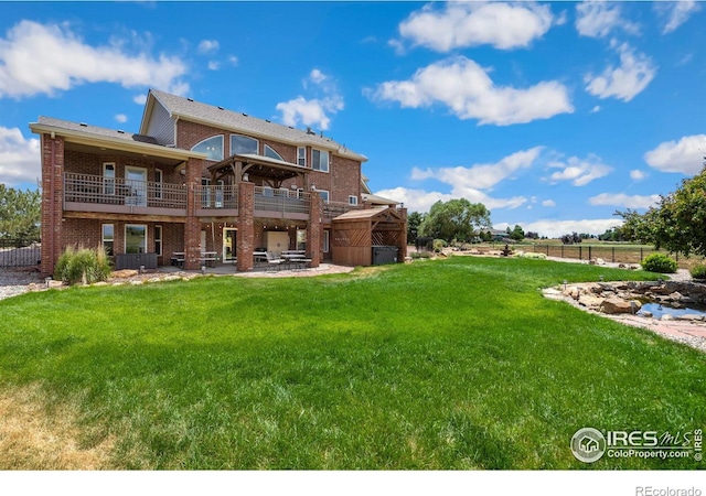 rear view of property featuring a balcony, a yard, and a patio