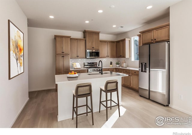 kitchen with sink, stainless steel appliances, an island with sink, decorative backsplash, and a breakfast bar