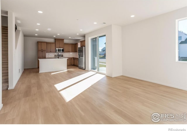 kitchen with appliances with stainless steel finishes, a center island, light hardwood / wood-style floors, and backsplash