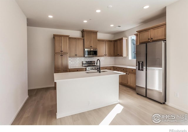 kitchen with tasteful backsplash, sink, an island with sink, and appliances with stainless steel finishes