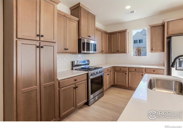 kitchen featuring decorative backsplash, stainless steel appliances, light hardwood / wood-style floors, and sink