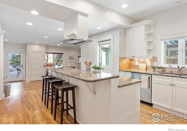 kitchen featuring dishwasher, sink, a kitchen island, light stone counters, and white cabinetry