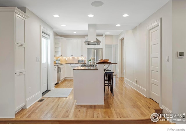 kitchen featuring a kitchen bar, stainless steel appliances, exhaust hood, a center island, and white cabinetry