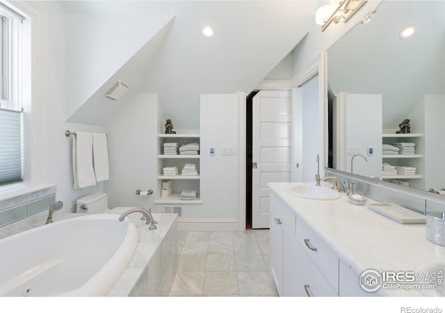 bathroom with tiled tub, vanity, and toilet