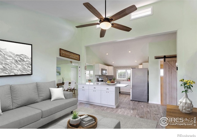 living room featuring a barn door, ceiling fan, high vaulted ceiling, and light wood-type flooring