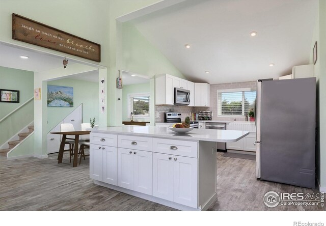 kitchen with decorative backsplash, light hardwood / wood-style floors, white cabinetry, and stainless steel appliances