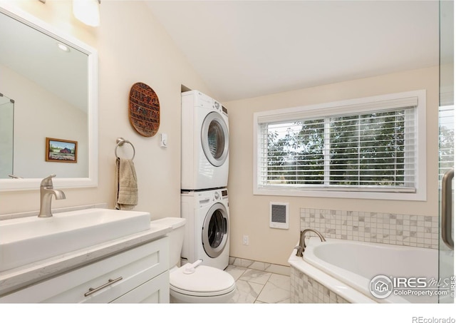 bathroom with stacked washing maching and dryer, vaulted ceiling, tiled tub, sink, and toilet