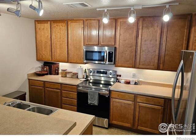 kitchen featuring sink, a textured ceiling, track lighting, decorative light fixtures, and appliances with stainless steel finishes