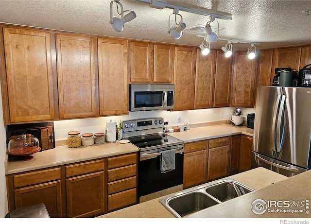 kitchen featuring a textured ceiling, stainless steel appliances, rail lighting, and sink