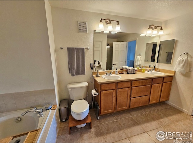 bathroom with tile patterned flooring, vanity, toilet, and tiled bath