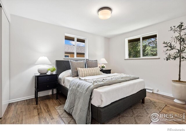 bedroom featuring a baseboard heating unit, baseboards, and wood finished floors