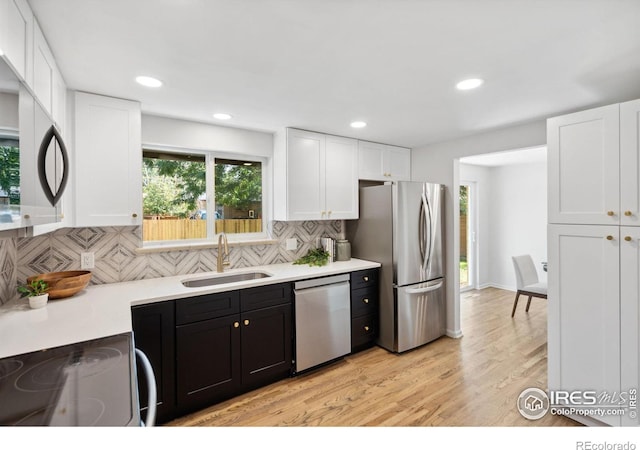 kitchen with white cabinets, light wood-style flooring, stainless steel appliances, light countertops, and a sink