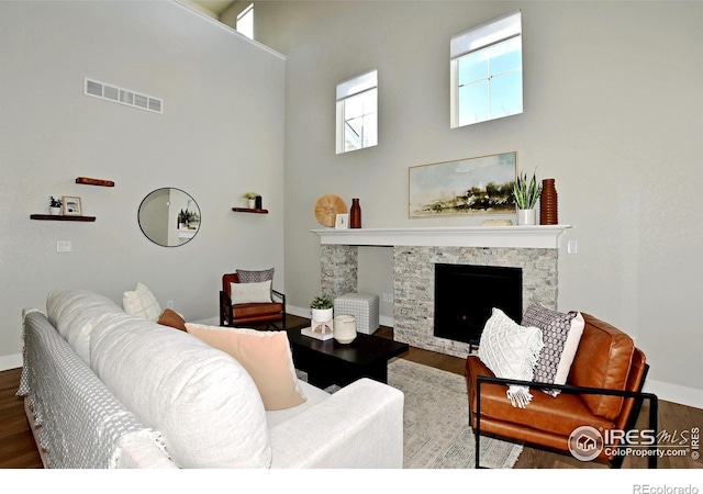 living room with hardwood / wood-style flooring, a stone fireplace, and a high ceiling