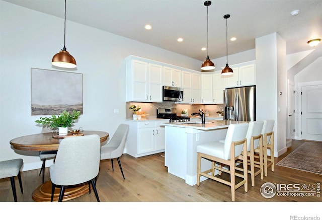 kitchen with a kitchen island with sink, white cabinets, appliances with stainless steel finishes, tasteful backsplash, and decorative light fixtures