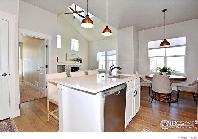 kitchen featuring stainless steel dishwasher, sink, a center island with sink, white cabinets, and hanging light fixtures