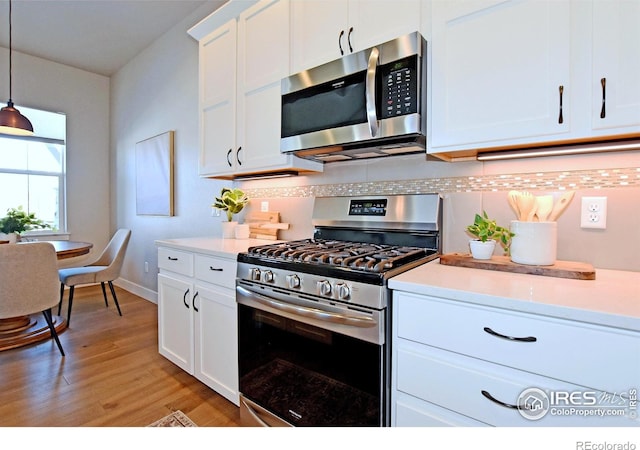 kitchen with decorative backsplash, white cabinets, stainless steel appliances, and decorative light fixtures