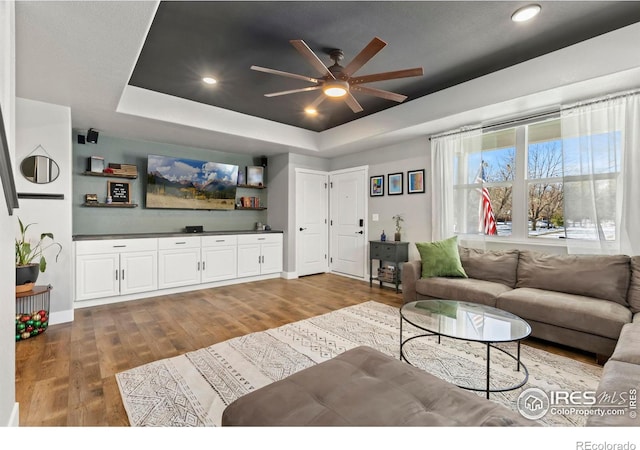 living room with wood-type flooring, a raised ceiling, and ceiling fan