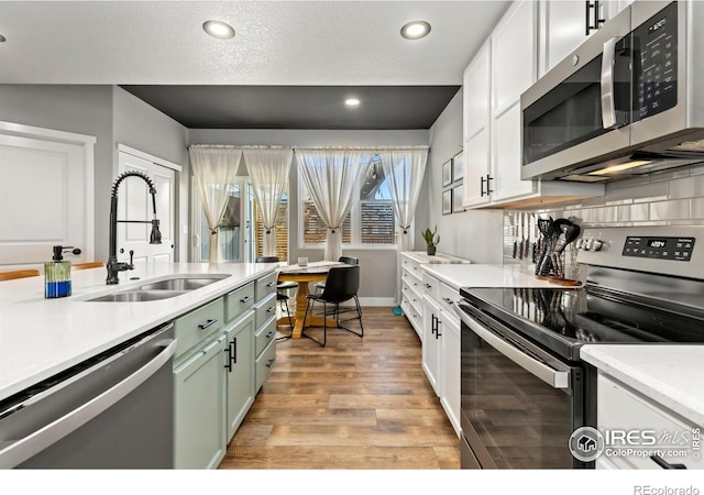 kitchen with sink, stainless steel appliances, green cabinets, light hardwood / wood-style flooring, and white cabinets