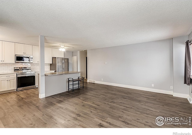 kitchen with dark wood-type flooring, a breakfast bar, white cabinetry, appliances with stainless steel finishes, and decorative backsplash