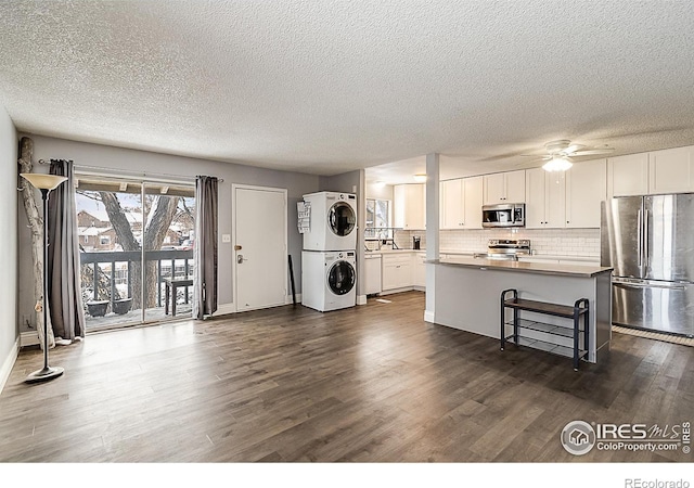 kitchen with decorative backsplash, appliances with stainless steel finishes, stacked washing maching and dryer, dark wood-style floors, and white cabinets