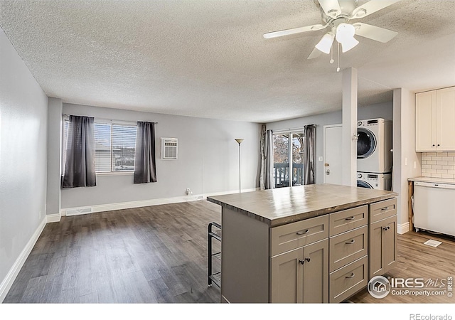 kitchen with a healthy amount of sunlight, stacked washing maching and dryer, dark wood-style flooring, dishwasher, and open floor plan