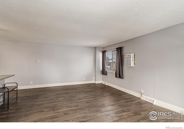 unfurnished room with an AC wall unit, baseboards, dark wood-style flooring, and a textured ceiling