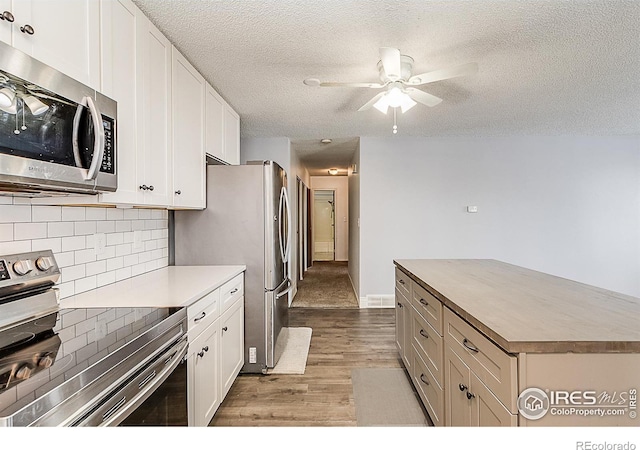 kitchen featuring light wood-type flooring, a textured ceiling, white cabinetry, appliances with stainless steel finishes, and decorative backsplash