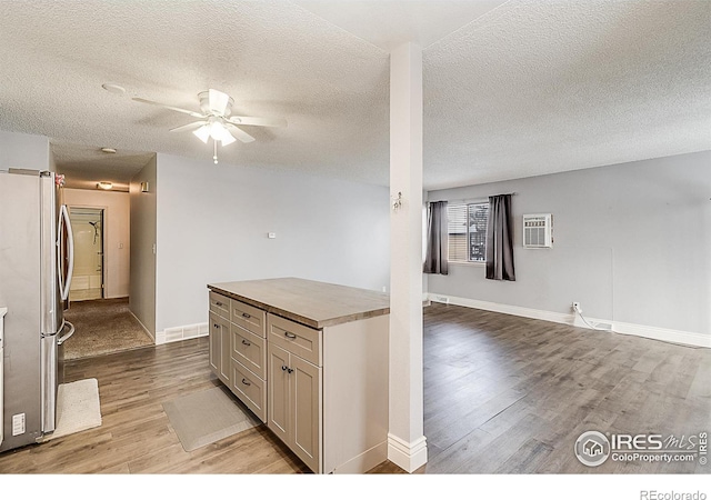 kitchen featuring a wall unit AC, baseboards, light wood-style flooring, freestanding refrigerator, and ceiling fan