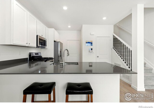 kitchen with kitchen peninsula, a kitchen breakfast bar, stainless steel appliances, white cabinets, and light hardwood / wood-style floors