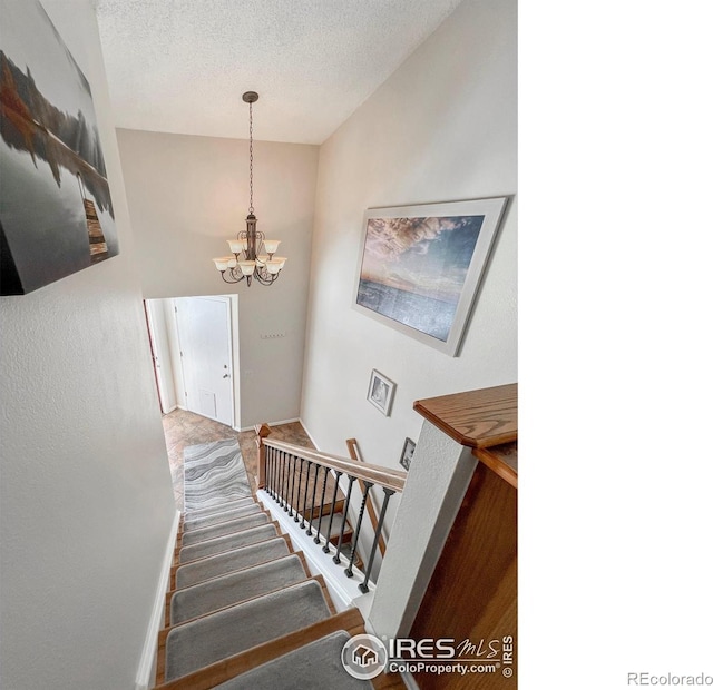 stairway featuring a textured ceiling and an inviting chandelier