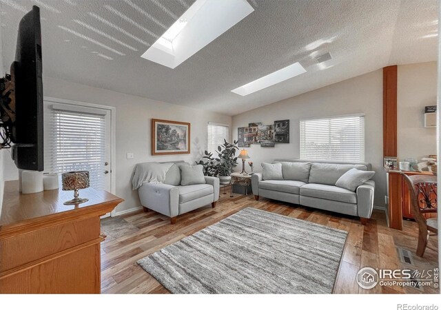 living room featuring lofted ceiling with skylight, a textured ceiling, and light hardwood / wood-style flooring