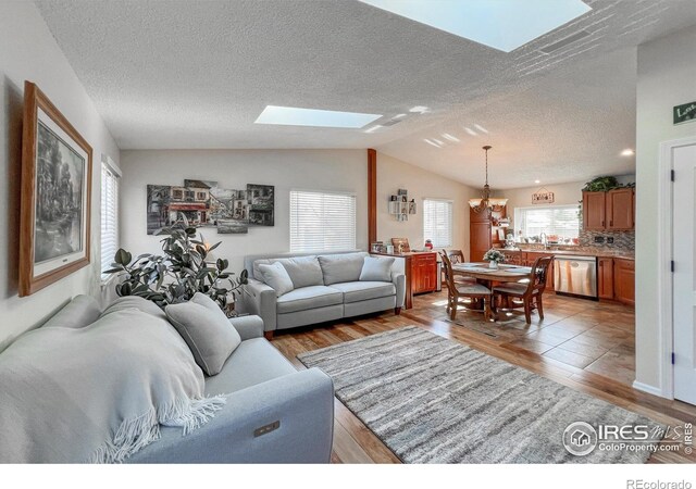 living room with hardwood / wood-style floors, lofted ceiling with skylight, a textured ceiling, and an inviting chandelier