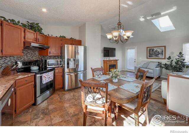 kitchen with tasteful backsplash, vaulted ceiling with skylight, stainless steel appliances, pendant lighting, and a chandelier