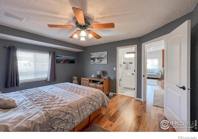 bedroom with a textured ceiling, ceiling fan, light hardwood / wood-style floors, and ensuite bathroom