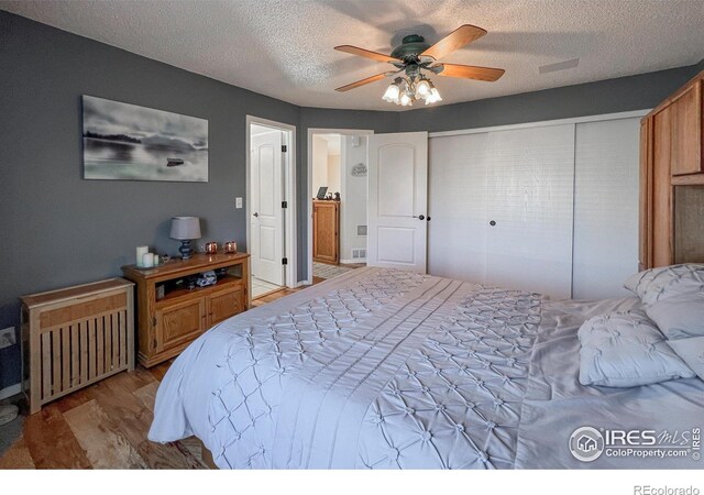 bedroom with ceiling fan, radiator heating unit, a textured ceiling, a closet, and light wood-type flooring