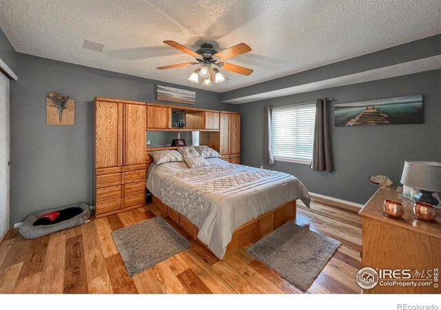 bedroom with ceiling fan, light hardwood / wood-style flooring, and a textured ceiling