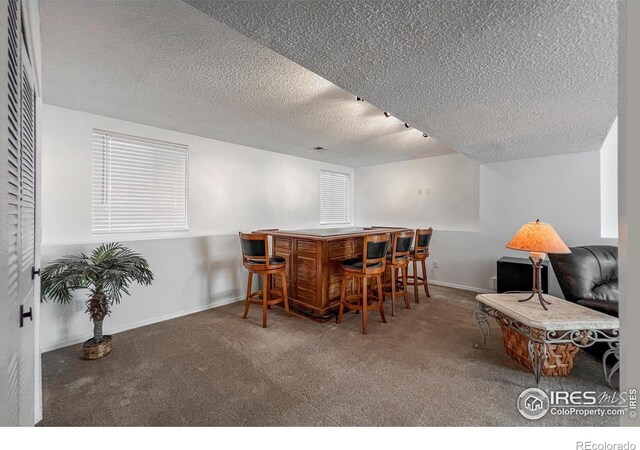 carpeted dining space featuring bar area and a textured ceiling