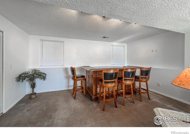 carpeted dining space with a textured ceiling and indoor bar