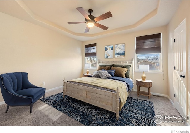 bedroom with ceiling fan, multiple windows, a raised ceiling, and carpet flooring