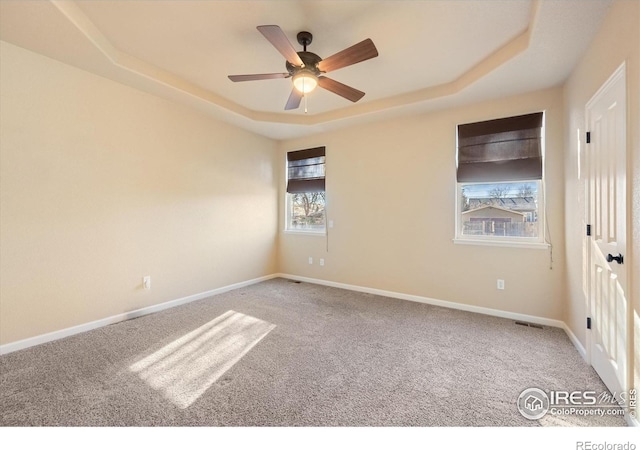 unfurnished room with ceiling fan, a tray ceiling, and carpet flooring