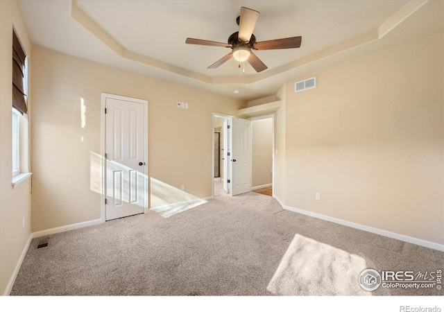 interior space with a closet, ceiling fan, a tray ceiling, and light carpet