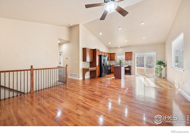 unfurnished living room featuring ceiling fan, light wood-type flooring, and high vaulted ceiling